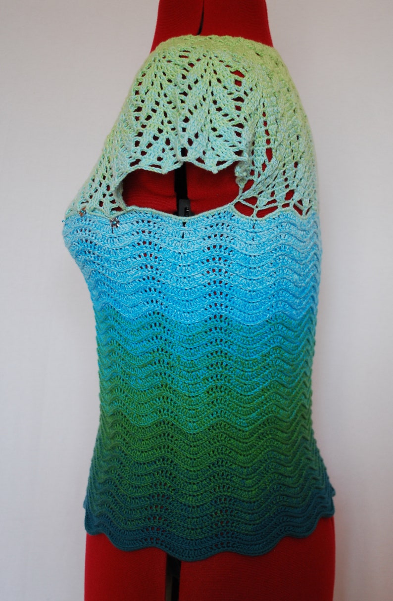May include: A crocheted top with a green, blue, and light green ombre design. The top has a scalloped hem and a lacy neckline.