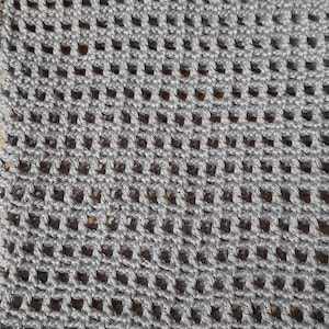 K&ouml;nnte beinhalten: Nahaufnahme eines grau geh&auml;kelten Stoffes mit einem netzartigen Muster. Das Garn ist einfarbig mittelgrau, und die Maschen bilden eine Reihe gleichm&auml;&szlig;ig verteilter quadratischer &Ouml;ffnungen. Die Textur ist sichtbar, was auf einen handgefertigten Artikel hindeutet.