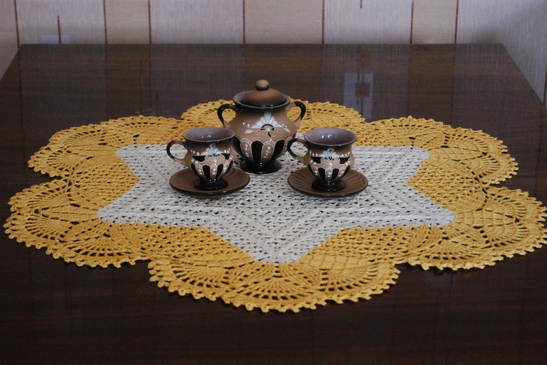 May include: A brown ceramic tea set with a teapot and two cups and saucers, set on a yellow and white crocheted doily.