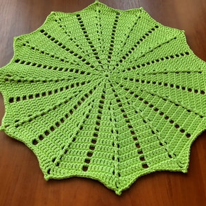May include: A green crocheted doily with a starburst pattern. The doily is made with a single crochet stitch and has a scalloped edge.