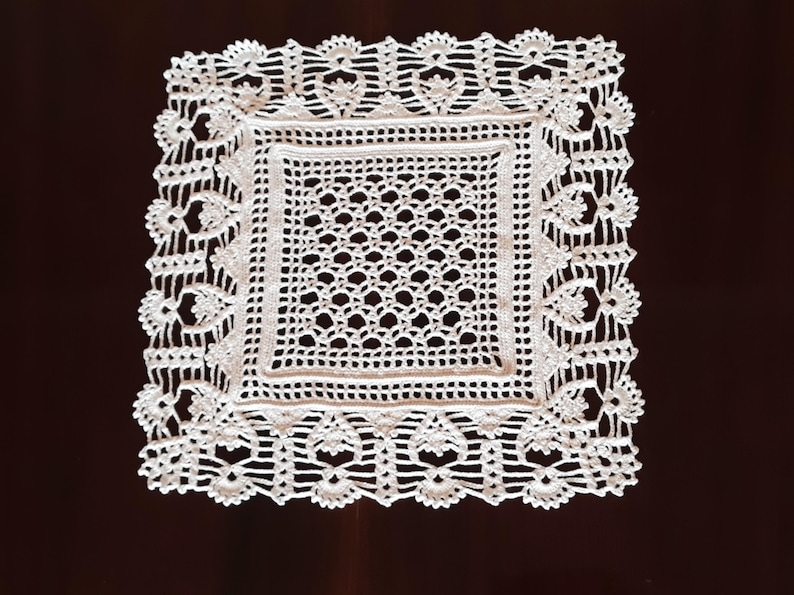 May include: White crocheted square doily with a delicate floral pattern around the border.