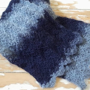 May include: A soft, blue and gray knitted scarf with a fuzzy texture. The scarf is made of a gradient yarn that transitions from a light blue to a dark blue.