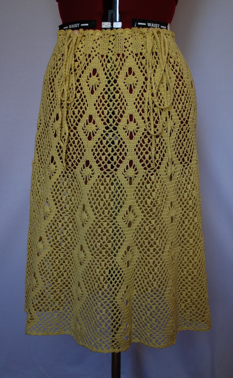 May include: A yellow crochet skirt with a delicate floral pattern. The skirt has a drawstring waist and a flowing, A-line silhouette.