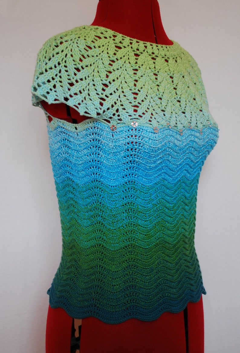 May include: A crocheted top with a green, blue, and turquoise ombre design. The top has a scalloped hem and a delicate crocheted neckline.