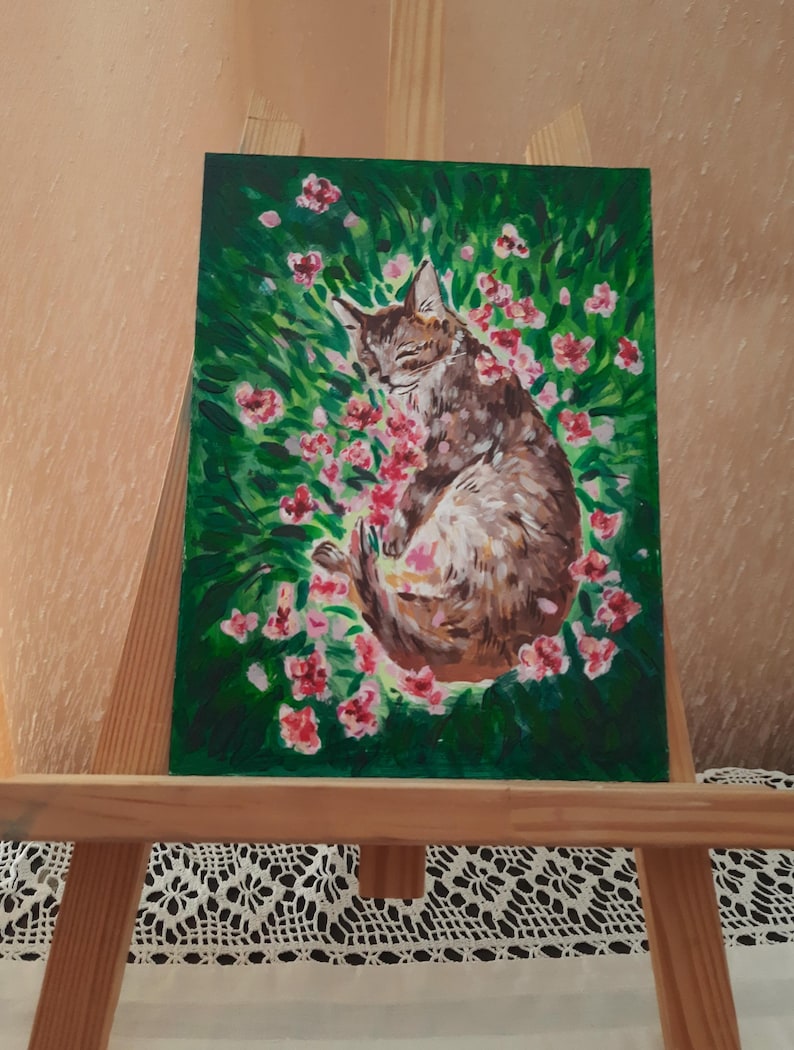 Puede incluir: Una pintura de un gato durmiendo en un campo de flores rosas. El gato es marr&oacute;n y blanco y tiene los ojos cerrados. Las flores est&aacute;n rodeadas de hierba verde.