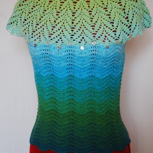May include: A crocheted top with a green, blue, and turquoise ombre design. The top has a scalloped hem and a delicate crocheted lace neckline. The top is adorned with small, silver sequins.