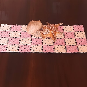 May include: A crocheted pink and beige table runner with a seashell on top.