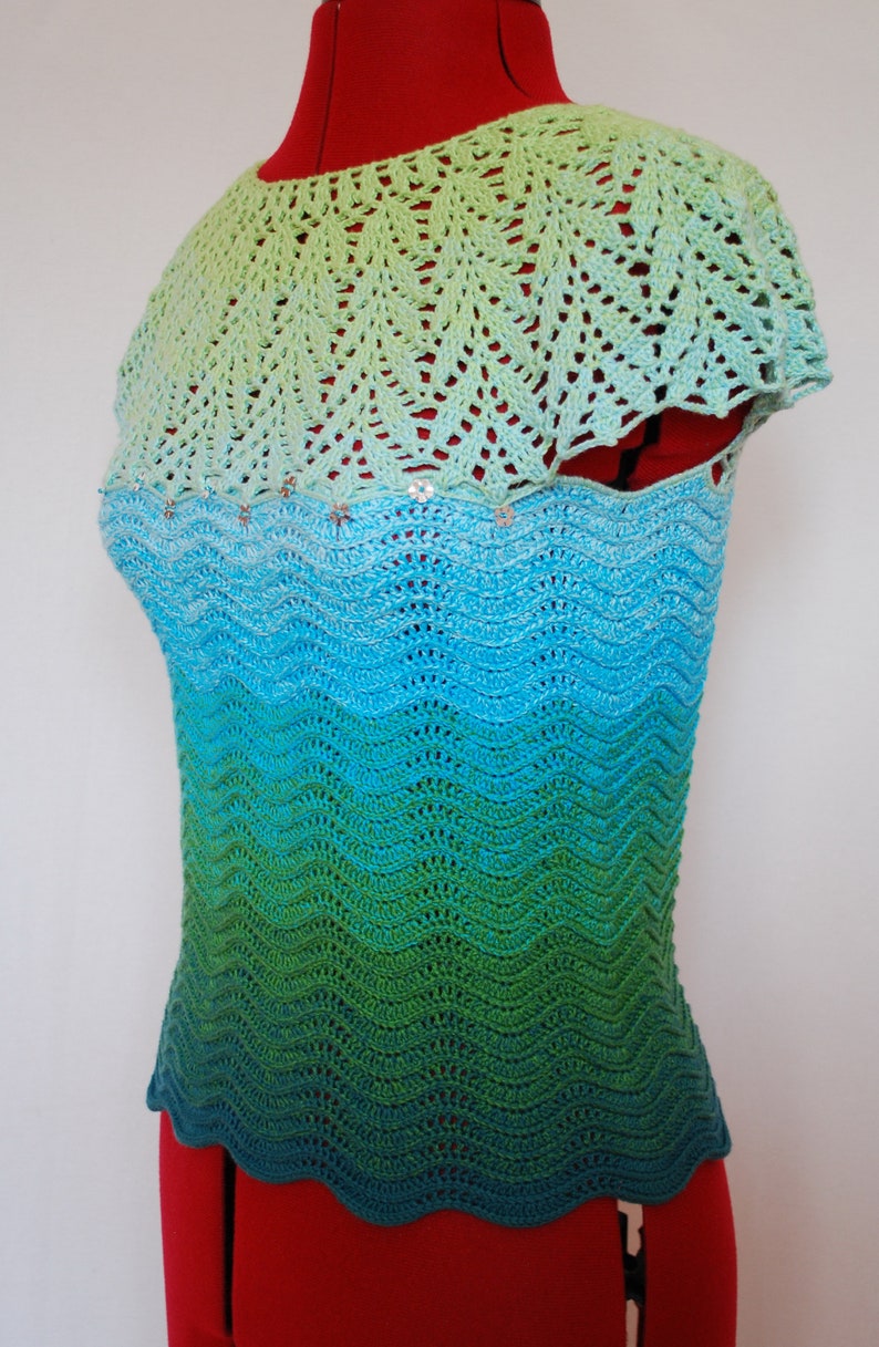 May include: A crocheted top with a green, blue, and turquoise ombre pattern. The top has a scalloped hem and a crocheted collar.