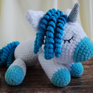 May include: A white crocheted unicorn with blue yarn mane and tail. The unicorn has closed eyes and a silver horn.