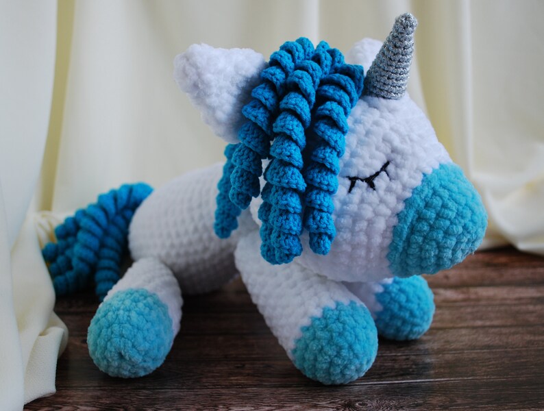 May include: A white crocheted unicorn with blue yarn mane and tail. The unicorn has closed eyes and a silver horn.