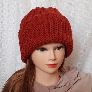 May include: A red knitted beanie with a slouchy fit. The beanie is made with a textured stitch pattern.