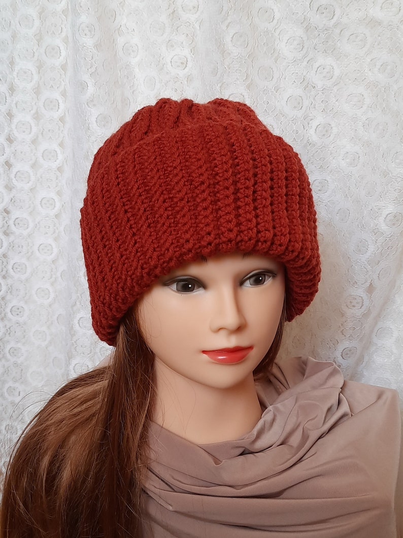 May include: A red knitted beanie with a slouchy fit. The beanie is made with a textured stitch pattern.