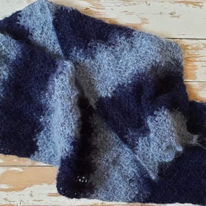 May include: A blue and gray fuzzy crocheted scarf with a scalloped edge.