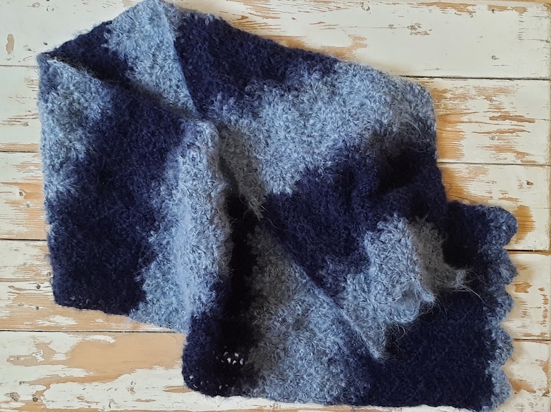 May include: A blue and gray fuzzy crocheted scarf with a scalloped edge.