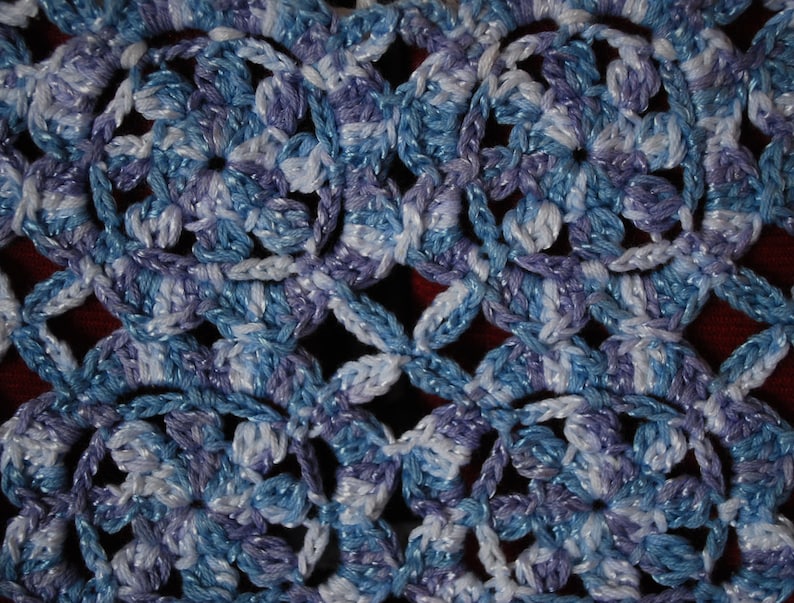 Puede incluir: Primer plano de una tela de crochet con un patr&oacute;n repetitivo de flores azules, blancas y moradas. La tela tiene un aspecto suave y texturizado.