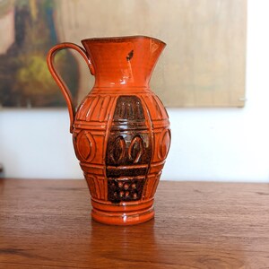 May include: A vintage orange and brown ceramic jug with a geometric design. The jug has a wide mouth and a handle.