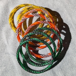 May include: A set of colourful glass bangles, featuring a yellow, orange, and green striped pattern. The bangles are stacked on top of each other, creating a visually appealing display.