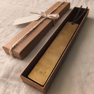 Peut inclure: Un marque-page en laiton avec les initiales "K ♡ T" gravées, présenté dans une boîte en carton marron. La boîte est attachée avec de la ficelle et comprend une étiquette vierge. Le marque-page a un cordon vert attaché.