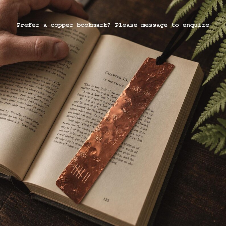 May include: A rectangular copper bookmark with a hammered, textured surface, featuring an etched cross and tally marks. The bookmark is attached to a black cord and rests on an open book page. Text on the image reads: Prefer a copper bookmark? Please message to enquire.