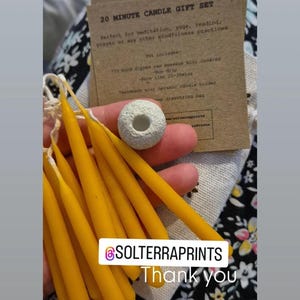 May include: A set of 20-minute beeswax candles in a small gift set. The set includes 10 hand-dipped candles, a ceramic candle holder, and a drawstring bag. The candles are yellow and the holder is white. The text on the card reads "20 Minute Candle Gift Set. Perfect for meditation, yoga, reading, prayer or any other mindfulness practices. Set includes: 10 hand dipped raw beeswax mini candles - non-drip - burn time 20-30mins. Handmade mini organic candle holder. Drawstring bag."