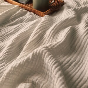 May include: A white textured blanket with a wicker tray holding a mug of coffee, a small bottle of essential oil, and a notebook with a drawing on it.