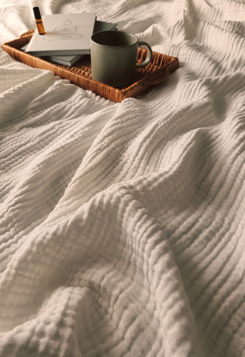 May include: A white textured blanket with a wicker tray holding a mug of coffee, a small bottle of essential oil, and a notebook with a drawing on it.