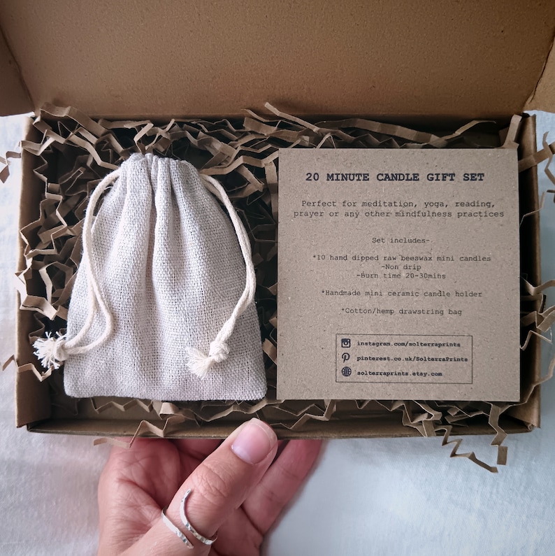 Op de afbeelding: Een 20 minuten durende kaars cadeau set in een kartonnen doos. De set bevat mini bijenwaskaarsen, een keramische kaarsenhouder en een katoenen trekkoordtas. De tekst op de kaart luidt: "Perfect voor meditatie, yoga, lezen, gebed of andere mindfulness praktijken."