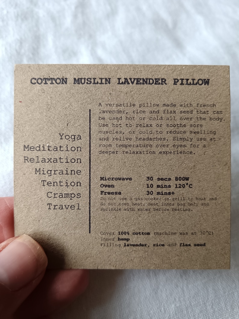 May include: A brown cotton muslin lavender pillow with the text "Cotton Muslin Lavender Pillow" printed on the front. The pillow is filled with lavender, rice, and flax seed. The text on the back of the pillow lists uses for the pillow, including yoga, meditation, relaxation, migraine, tension, cramps, and travel. The text also lists heating and cooling instructions for the pillow, including microwave, oven, and freezer times.