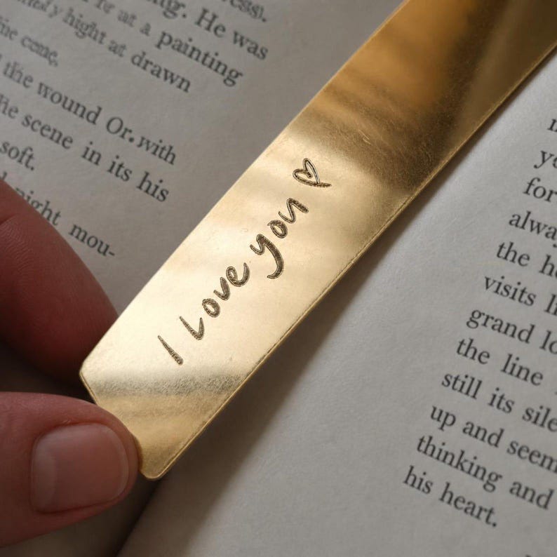 Peut inclure: Un marque-page rectangulaire en m&eacute;tal dor&eacute; &agrave; la surface lisse et r&eacute;fl&eacute;chissante. Le texte "I love you" est grav&eacute; dans le m&eacute;tal dans une police simple en minuscules, suivi d'un petit symbole de c&oelig;ur dessin&eacute; &agrave; la main pr&egrave;s du bord sup&eacute;rieur.