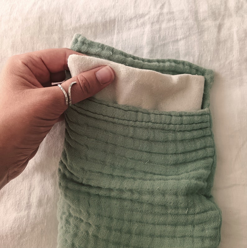 May include: A green quilted fabric pouch with a white fabric lining. The pouch is folded open, revealing the lining.