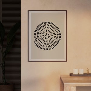 May include: A framed print with a black and white abstract design of a circle with a pattern of small ovals. The print is on a beige background and is framed in a brown frame.