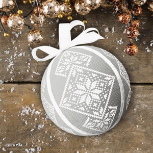 May include: A white Christmas bauble with a snowflake pattern on a wooden background with a white ribbon.