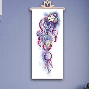 Op de afbeelding: Een witte canvas print met een aquarel illustratie van een roze en paarse droomvanger met veren en bloemen. De print hangt aan een lichtblauwe muur.