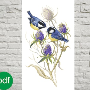 Op de afbeelding: Borduurpatroon met twee blauwe vogels met gele borst die op een tak zitten met paarse distelbloemen.