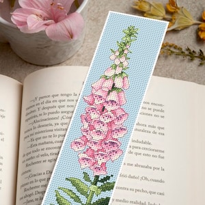 Può includere: Un segnalibro con un fiore di digitale rosa e verde su uno sfondo blu chiaro. Il segnalibro è fatto di tessuto e ha un design cucito.