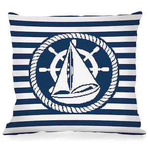 Pode incluir: Uma almofada de rayas brancas e azuis com um design náutico. O design apresenta um veleiro branco com um volante azul dentro de um círculo de corda.