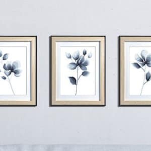Puede incluir: Tres impresiones enmarcadas con un diseño de estilo acuarela de flores azules sobre un fondo blanco. Los marcos son de madera clara con un borde exterior negro.