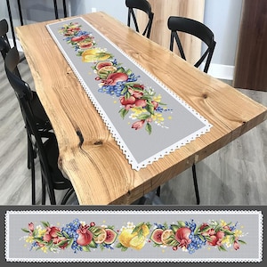 Puede incluir: Un camino de mesa gris con un borde de crochet blanco presenta un diseño bordado colorido de limones, granadas e higos. El camino de mesa se muestra en una mesa de madera.