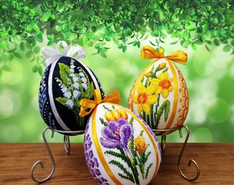 Può includere: Tre uova di Pasqua ricamate su supporti decorativi. Le uova sono decorate con diversi motivi floreali: gigli, narcisi e crochi. Le uova sono bianche, blu e viola.