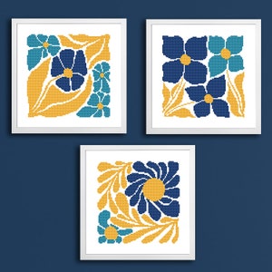 May include: Three framed cross-stitch embroidery designs featuring stylized floral patterns in shades of blue, teal, and yellow.