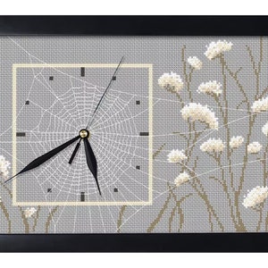 May include: A gray and white cross-stitch clock with a spiderweb design and white flowers. The clock hands are black and the clock face is surrounded by a white frame.