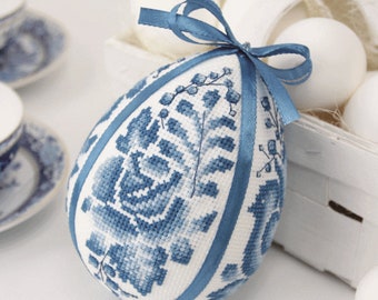 Può includere: Un uovo di Pasqua bianco decorato con un motivo floreale blu e un nastro blu.