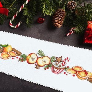 Può includere: Un runner da tavolo bianco con un design a tema natalizio con mele rosse, fette d'arancia, bastoncini di cannella e una tazza con una canna da zucchero. Il design è ricamato sul runner.