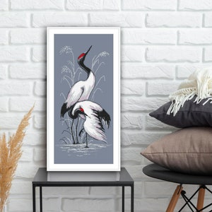 May include: A framed print depicting three white cranes with black wing tips and red accents standing in a marsh with tall grasses. The background is a light blue colour.