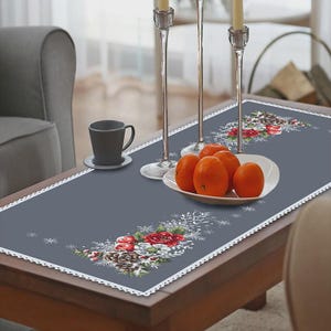 Peut inclure: Chemin de table gris avec une bordure en dentelle blanche et un motif floral avec des roses rouges, des pommes de pin et des flocons de neige. Sur une table basse en bois, avec une assiette d'oranges, une tasse et des bougeoirs.