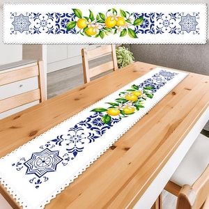 Peut inclure: Chemin de table blanc avec un motif géométrique bleu et blanc et un motif de citron et de fleurs. Le chemin de table est placé sur une table en bois clair. Le chemin de table a un bord festonné.
