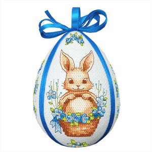 Könnte beinhalten: Ein weißes Osterei mit einem blauen Band und einem braunen Hasen, der einen Korb mit blauen Blumen hält.