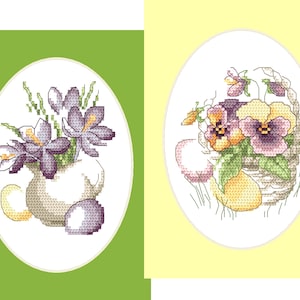 Puede incluir: Dos diseños de punto de cruz sobre un fondo verde y amarillo. Uno presenta flores moradas en un jarrón blanco con huevos. El otro muestra una cesta de pensamientos y huevos. Los diseños están enmarcados en óvalos blancos.