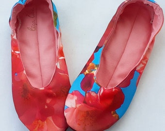 May include: A pair of floral print ballet flats with a pink interior. The flats have a blue background with red and pink flowers. The text "Liza Liza" is printed on the inside of one of the flats.