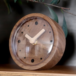 May include: A wooden clock with a clear face and black markings. The clock has a simple design with a single hand.